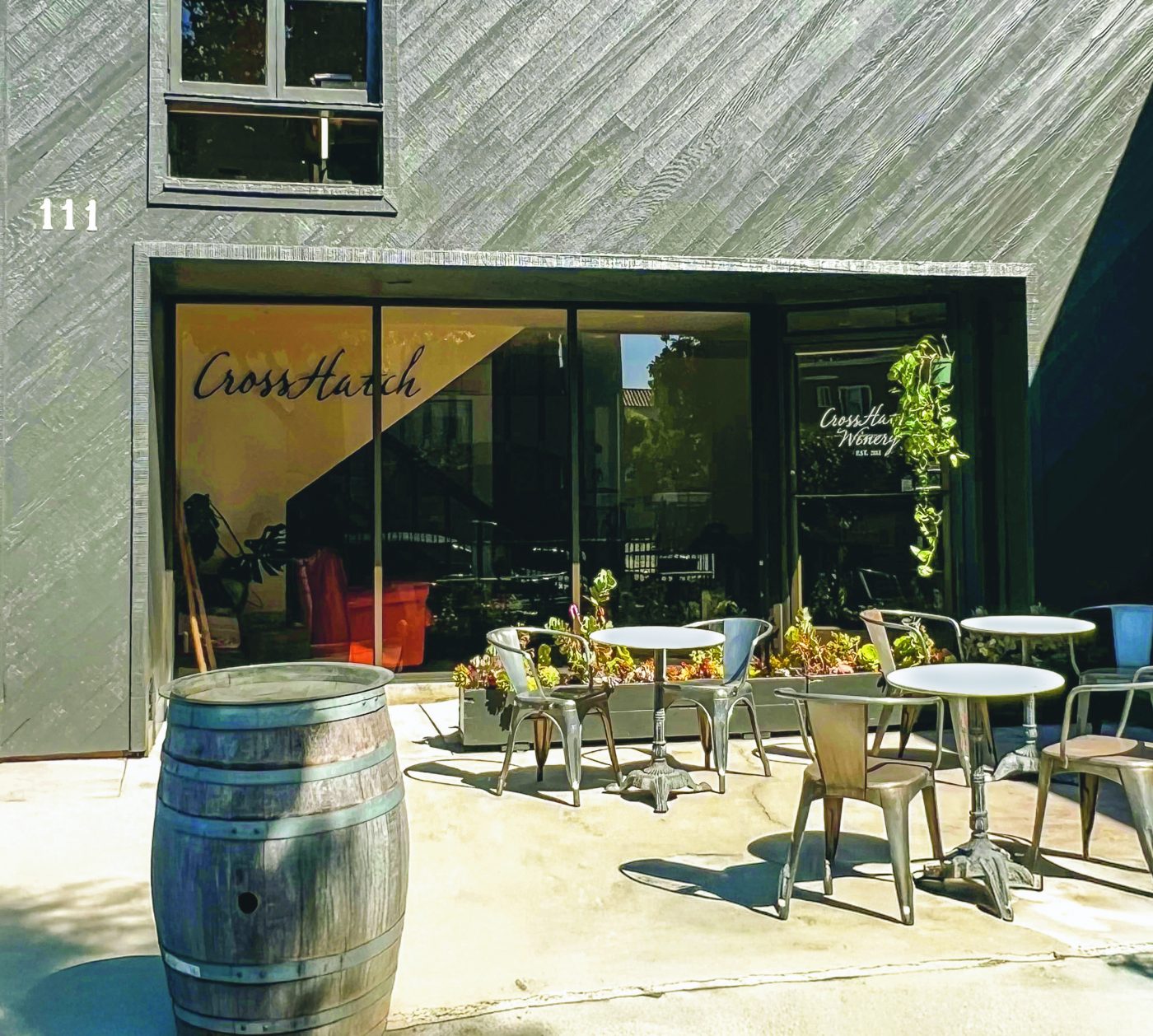 the front of CrossHatch Winery's wine tasting room in Santa Barbara. a dark front with a big glass window and some seating outside on a patio