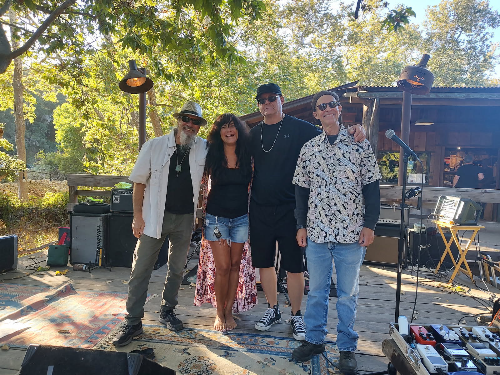 The Paradise Kings Band standing on a wood stage outside under the trees.